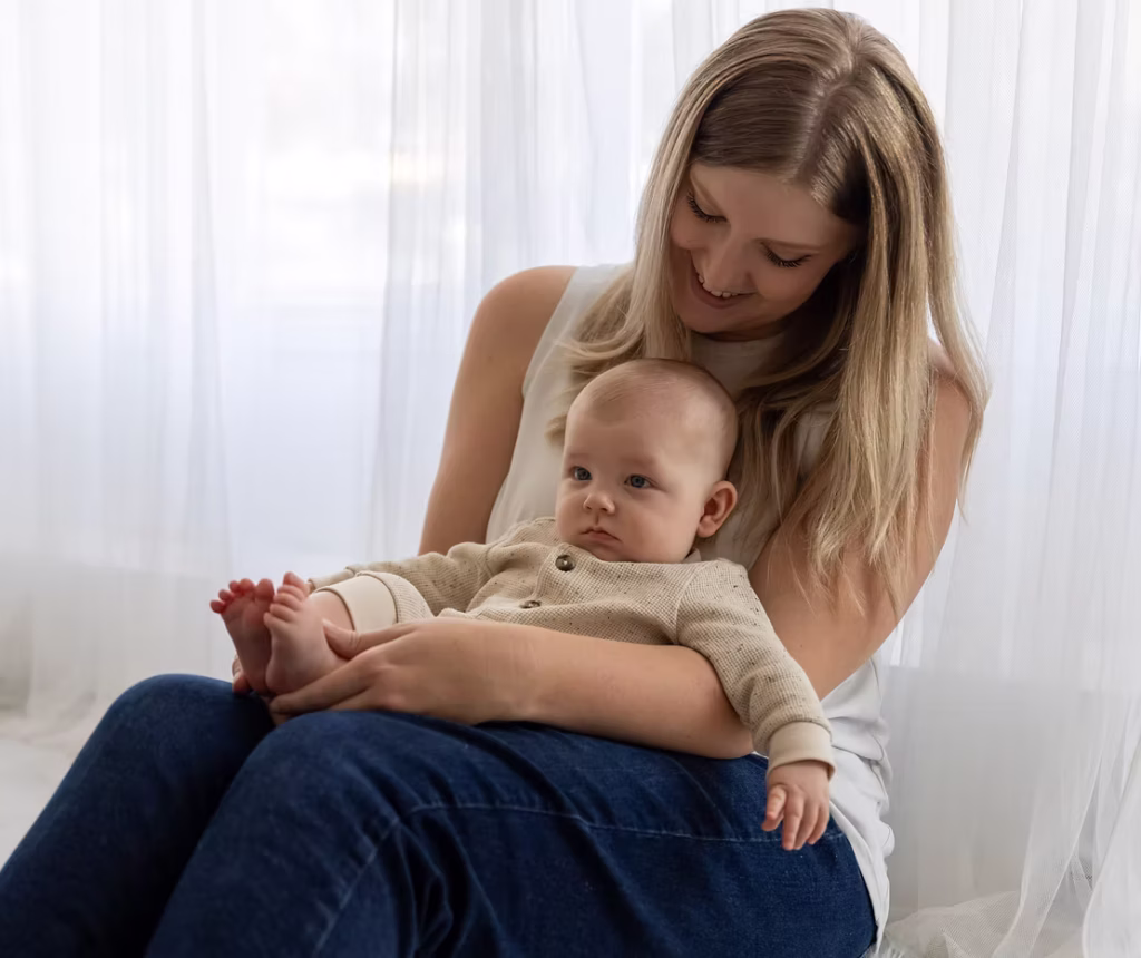 A mother and baby cuddle together in front of the studio's white and bright curtains